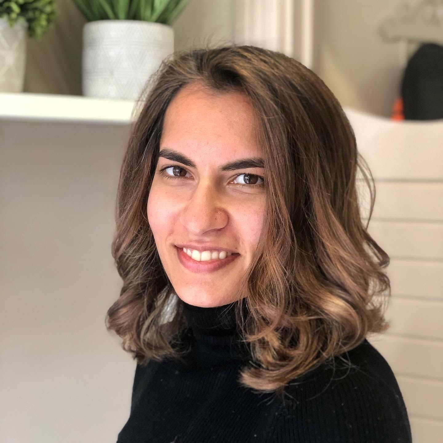 Smiling client with shoulder-length brown hair, caramel highlights and soft waves