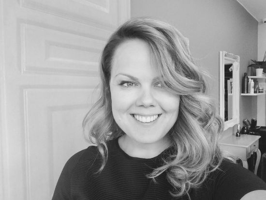 Black and white portrait of Emilia, founder and lead stylist, smiling with shoulder-length wavy hair and a dark top