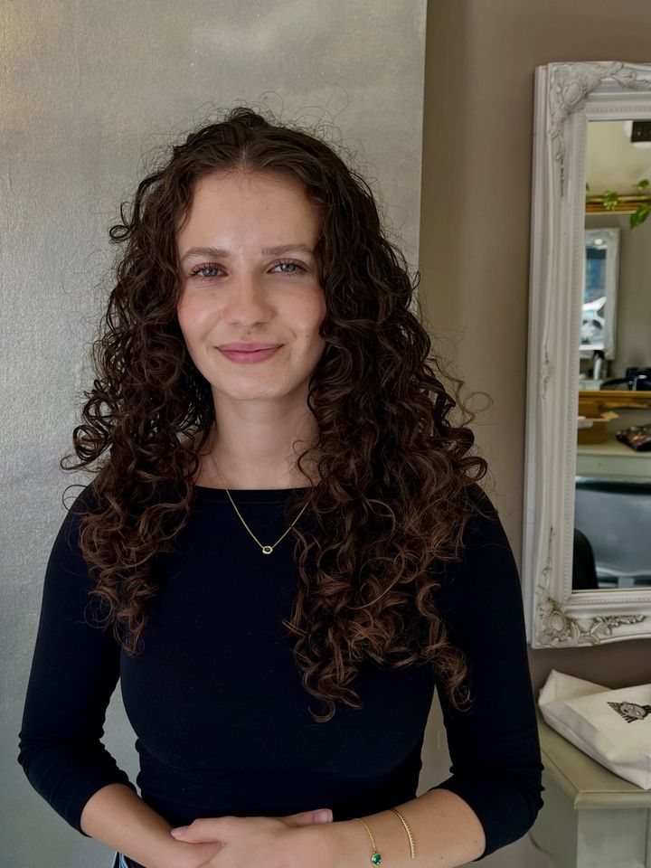 Smiling client with long, dark natural curls in front of a salon mirror