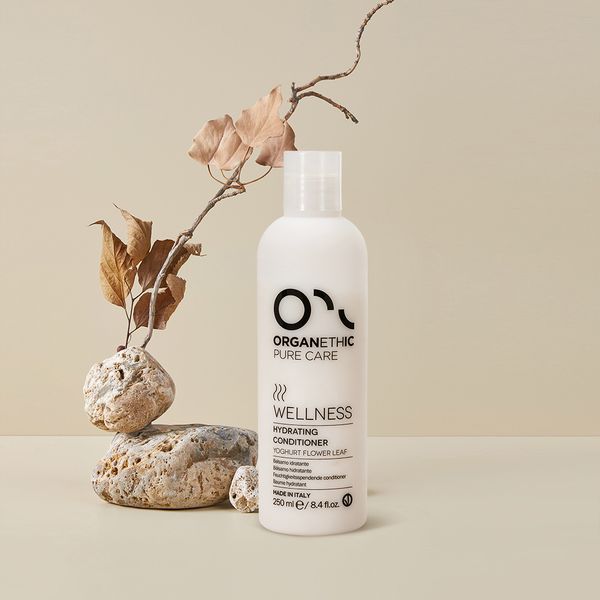 Organethic Pure Care Wellness Hydrating Conditioner, a white bottle on pale stones beside dried leaves