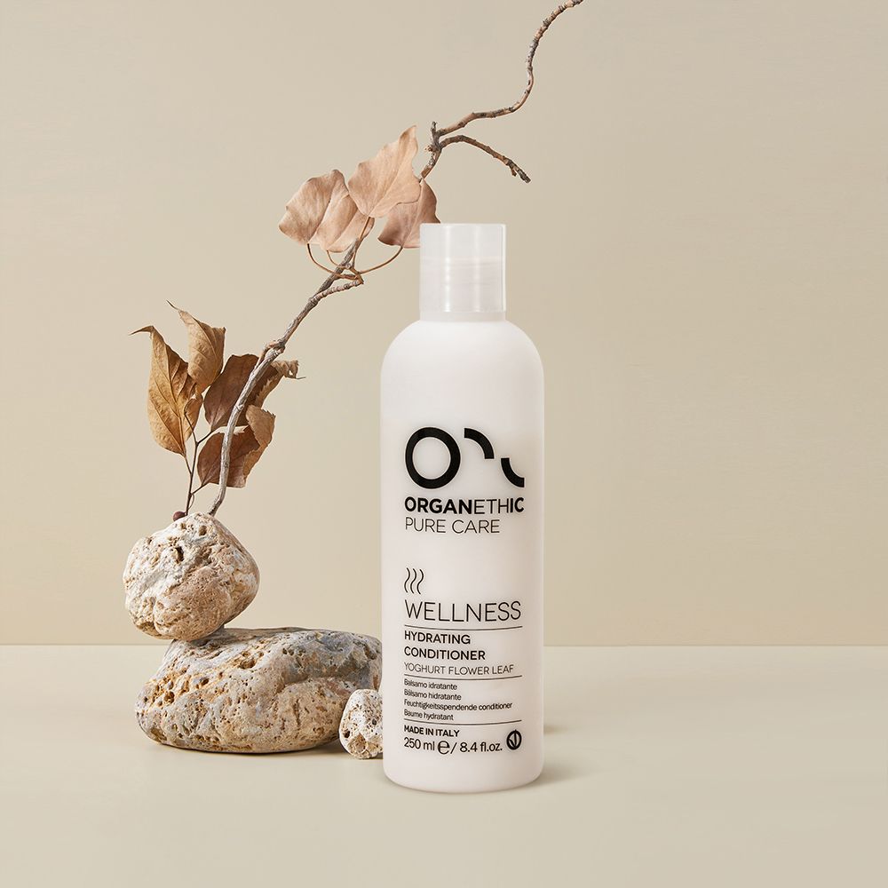 Organethic Pure Care Wellness Hydrating Conditioner, a white bottle on pale stones beside dried leaves