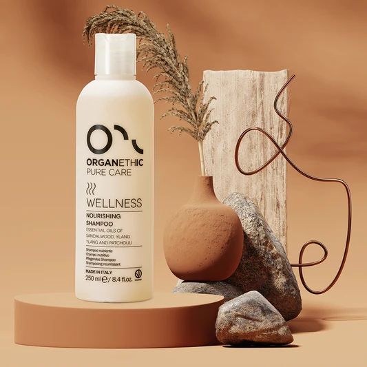 Organethic Pure Care Wellness Nourishing Shampoo, a white bottle on a terracotta stand with dried grasses and stones